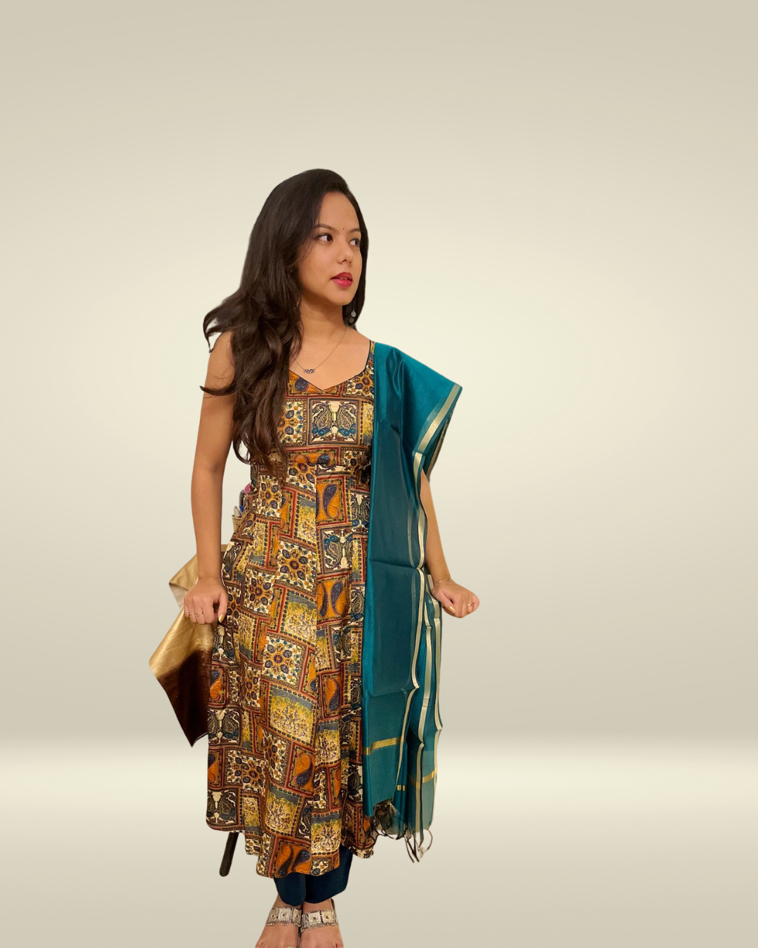 Woman holding a patterned dress and a green dupatta against a plain background