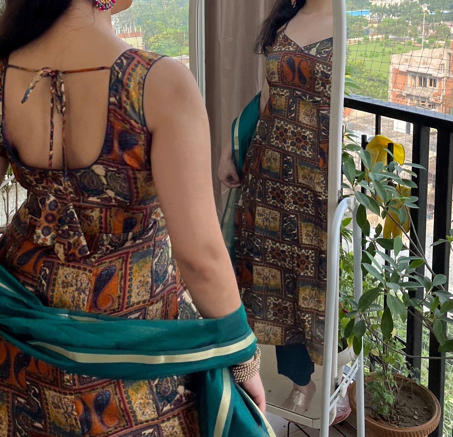 Woman wearing a patterned dress with a green dupatta, standing on a balcony.